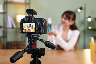 Photo of Beauty blogger recording video while talking about cosmetic products at home, focus on camera