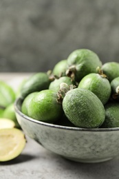 Photo of Fresh green feijoa fruits in bowl on light grey table, closeup