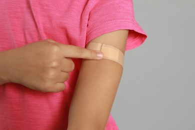 Photo of Vaccinated little girl showing medical plaster on her arm against light grey background, closeup