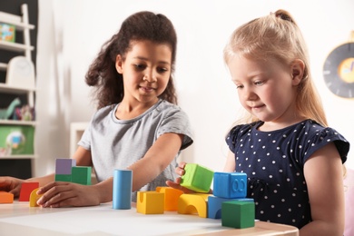 Photo of Cute little children playing with building blocks in kindergarten. Indoor activity