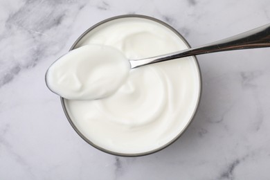 Photo of Delicious natural yogurt in bowl and spoon on white marble table, top view