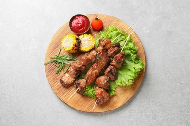 Photo of Wooden board with barbecued meat, garnish and sauce on grey background, top view