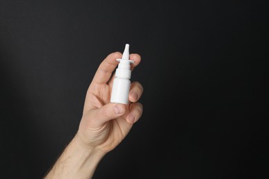 Photo of Man holding nasal spray on black background, closeup. Space for text