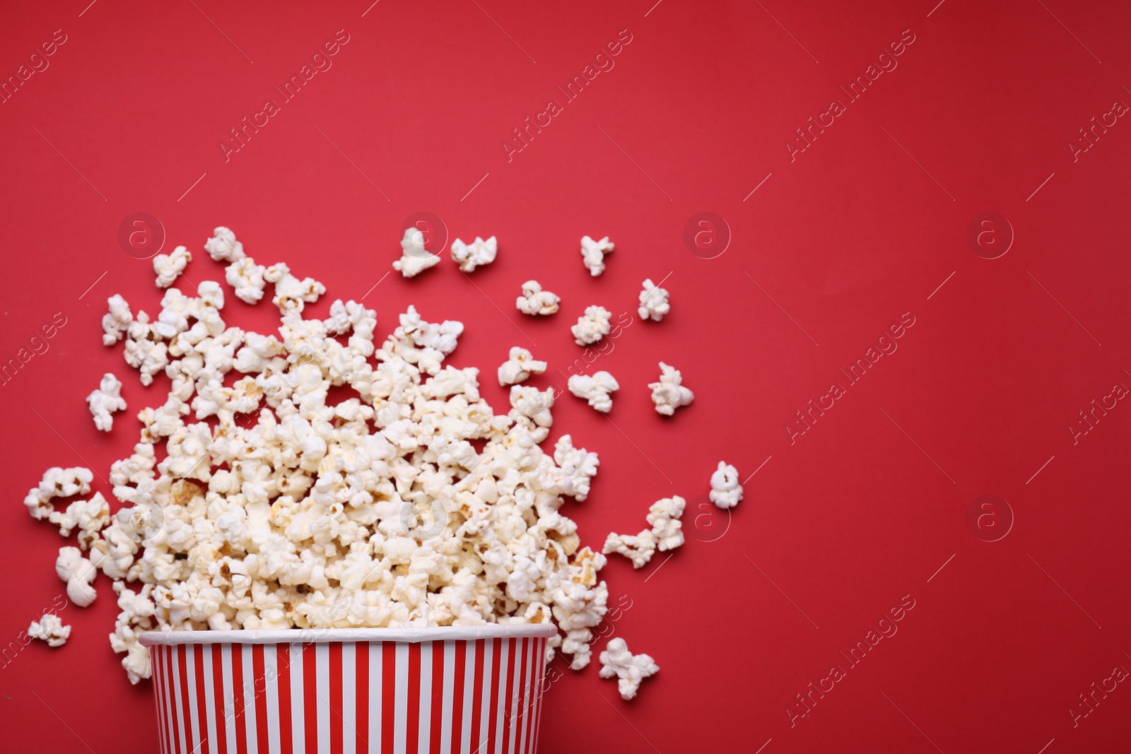 Photo of Overturned paper bucket with delicious popcorn on red background, flat lay. Space for text