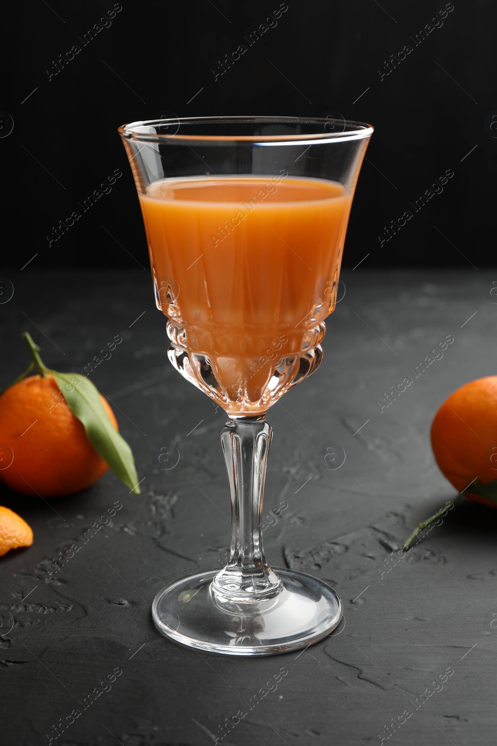 Photo of Tasty tangerine liqueur in glass and fresh fruits on black textured table
