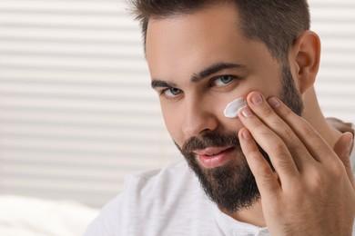 Photo of Man with dry skin applying cream onto his face on light background, space for text