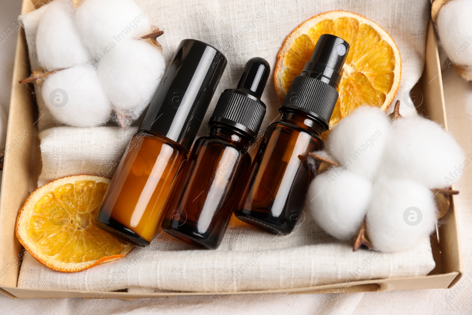 Photo of Bottles of organic cosmetic products, dried orange slices and cotton flowers in box, closeup