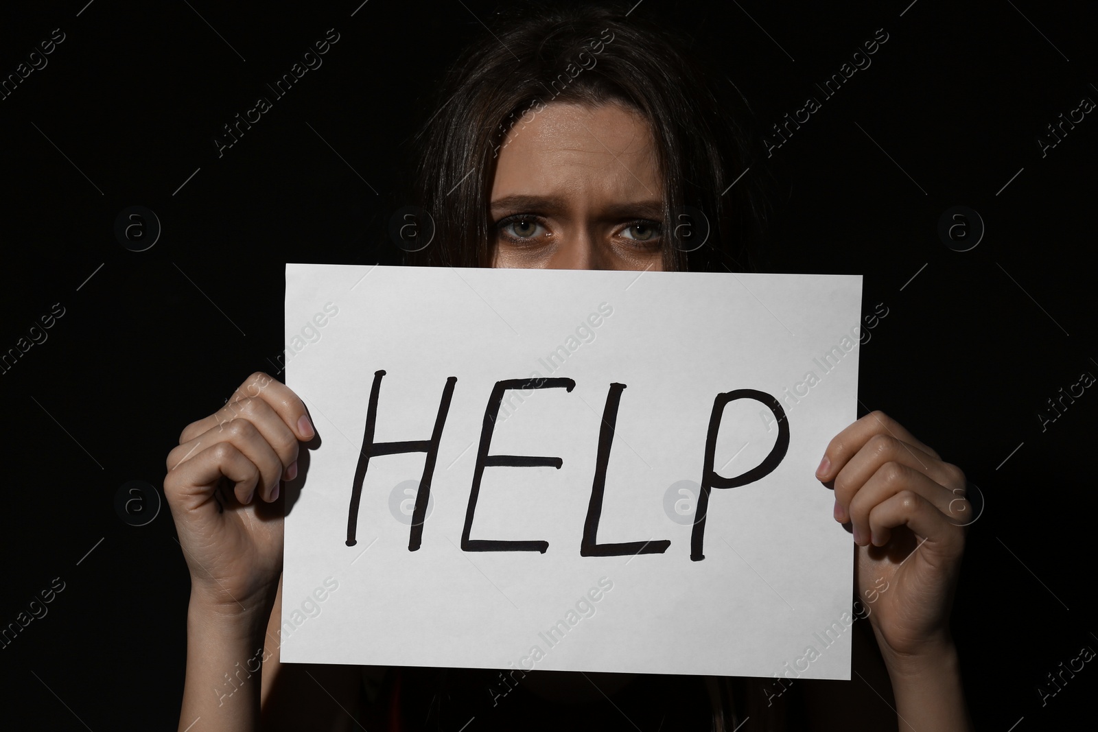 Photo of Abused young woman with sign HELP on black background. Domestic violence concept