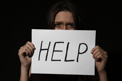 Photo of Abused young woman with sign HELP on black background. Domestic violence concept