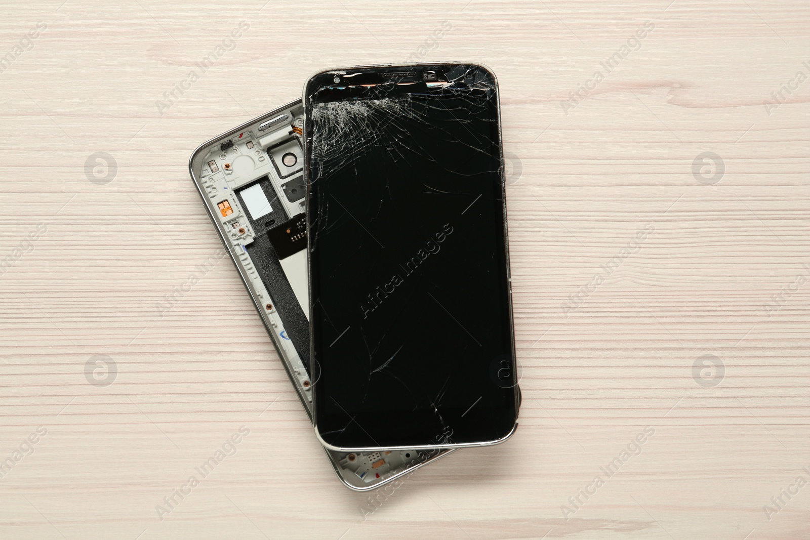 Photo of Damaged smartphone on wooden table, top view. Device repairing