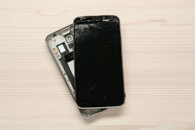 Photo of Damaged smartphone on wooden table, top view. Device repairing