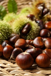 Photo of Fresh sweet edible chestnuts on wicker mat, closeup