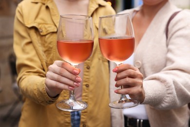 Photo of Women clinking glasses with rose wine outdoors, closeup