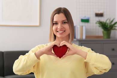 Young woman holding red heart indoors. Volunteer concept