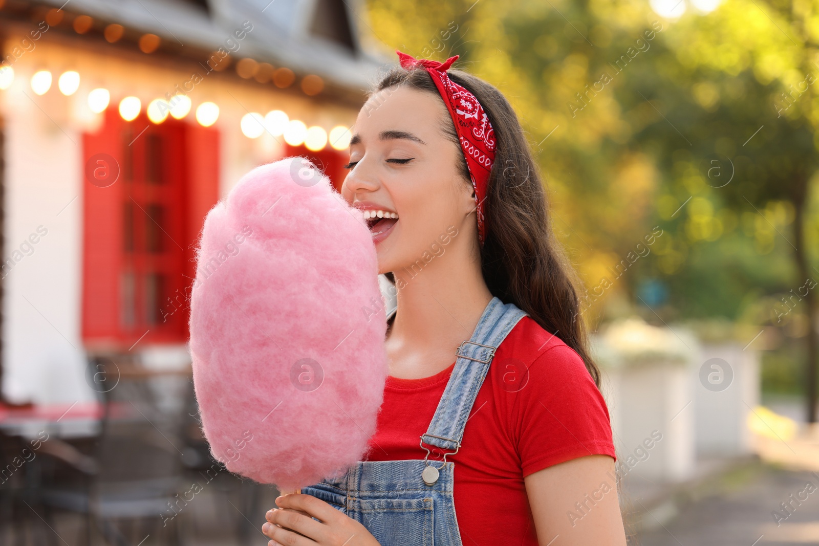 Photo of Stylish young woman eating cotton candy outdoors