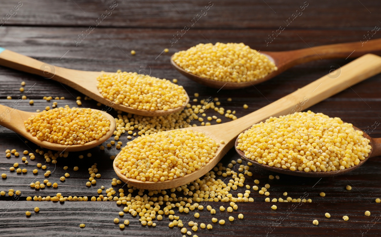 Photo of Spoons with millet groats on wooden table, closeup