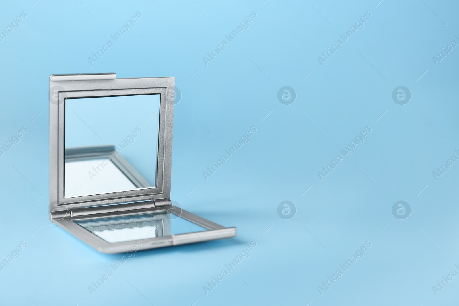 Photo of Stylish cosmetic pocket mirror on light blue background. Space for text
