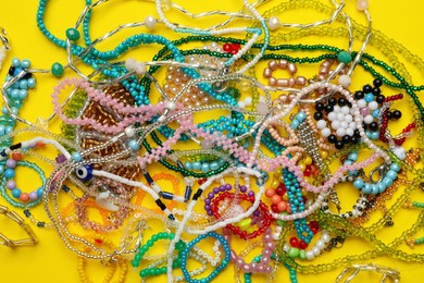 Photo of Pile of beautiful handmade beaded jewelry on yellow background, top view