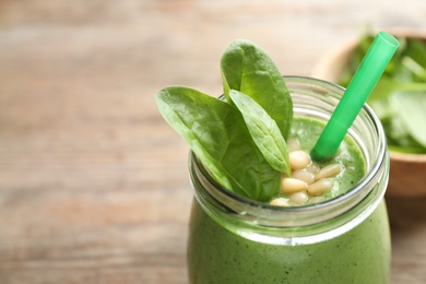 Jar of healthy green smoothie with fresh spinach on wooden table, closeup view. Space for text