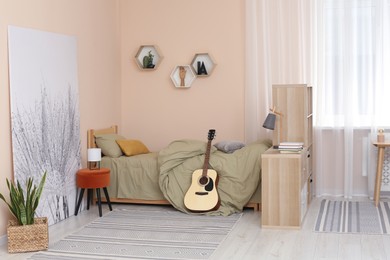Stylish teenager's room interior with comfortable bed and guitar