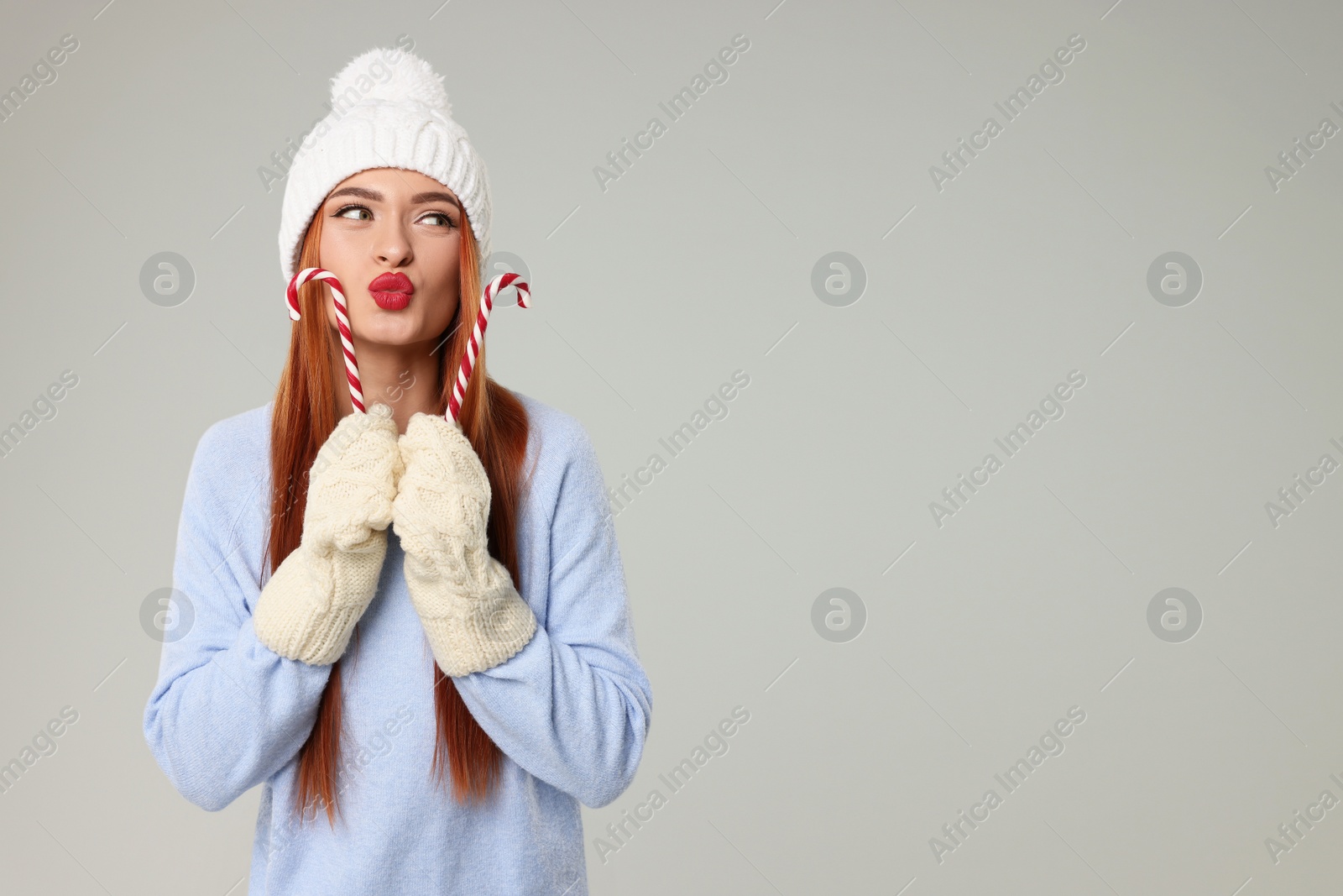 Photo of Young woman in hat and sweater with candy canes on light grey background, space for text. Christmas celebration