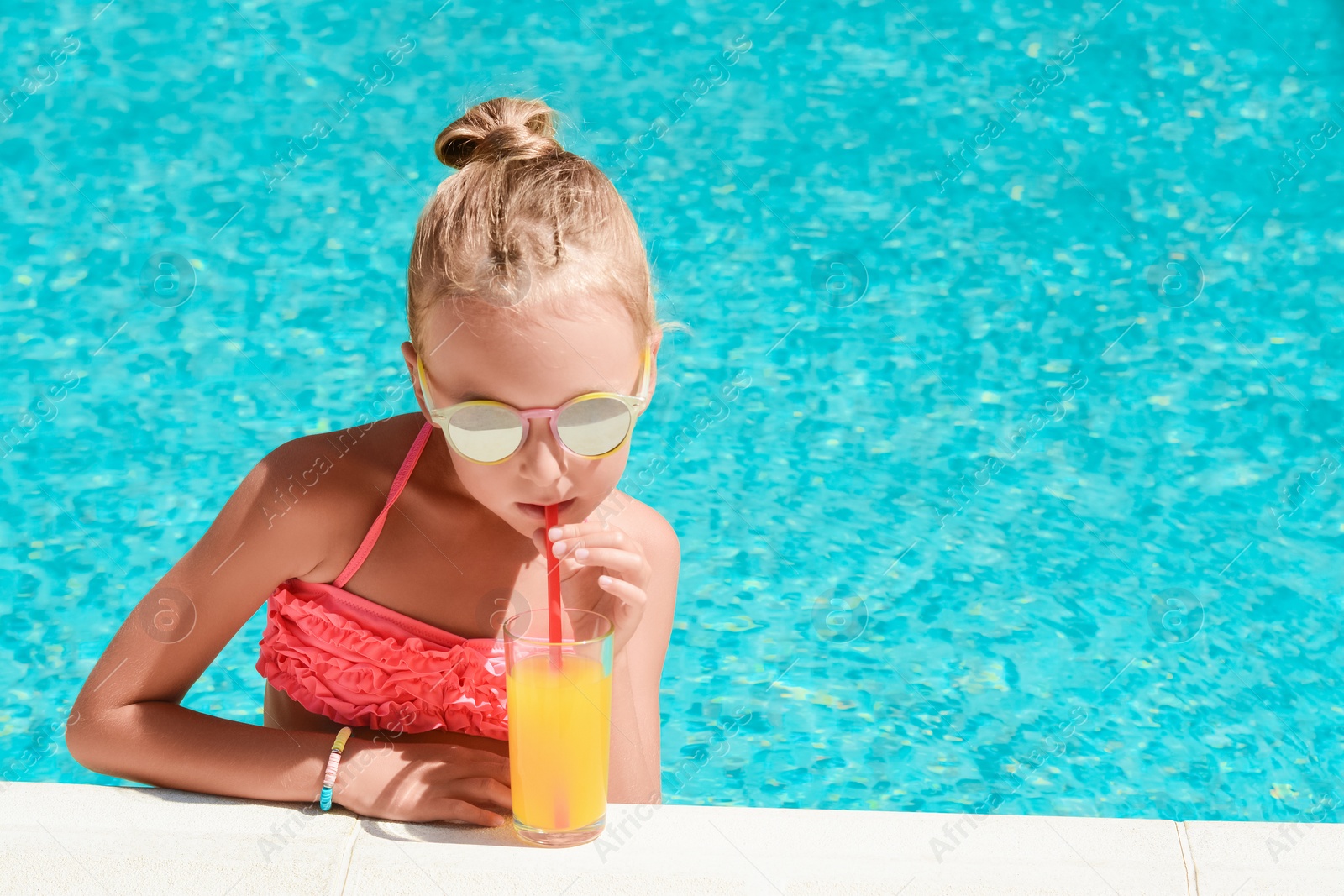 Photo of Cute little girl with glass of juice in swimming pool on sunny day. Space for text