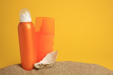 Photo of Sand with bottles of sunscreens and seashell against orange background, space for text. Sun protection