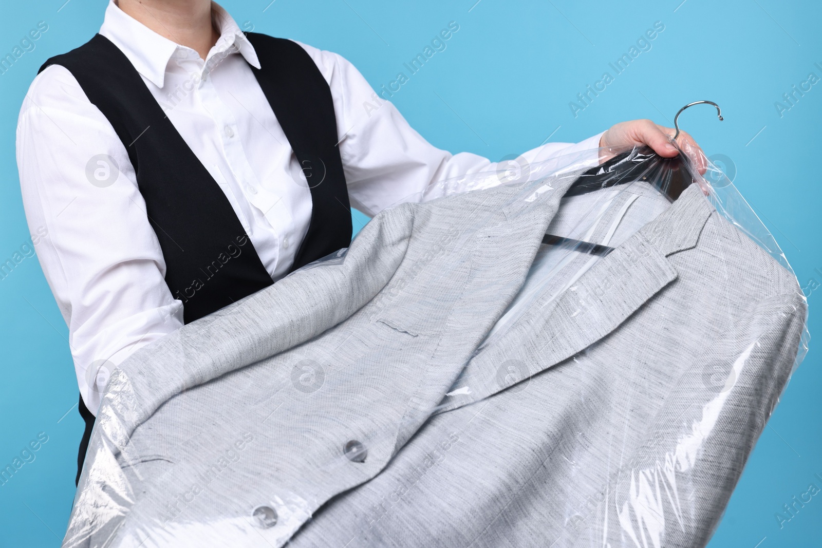 Photo of Dry-cleaning service. Woman holding jacket in plastic bag on light blue background, closeup