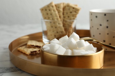 Photo of Refined sugar cubes in bowl and aromatic tea on white marble table, closeup