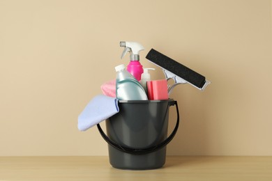 Bucket with different cleaning supplies on wooden floor near beige wall