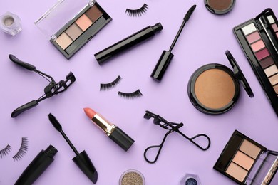 Photo of Eyelash curlers and makeup products on violet background, flat lay
