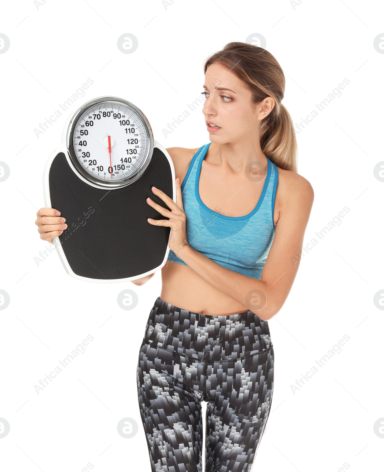 Photo of Worried young woman in sportswear holding bathroom scales on white background. Weight loss diet
