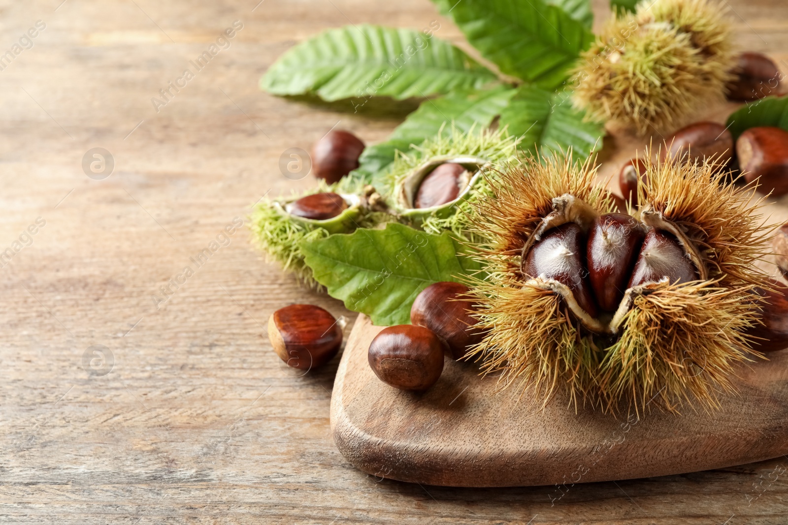 Photo of Fresh sweet edible chestnuts on wooden table. Space for text