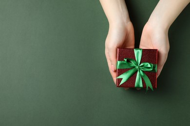 Photo of Woman holding beautifully wrapped Christmas gift box on dark green background, top view. Space for text