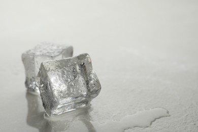 Crystal clear ice cubes with water drops on grey table, closeup. Space for text