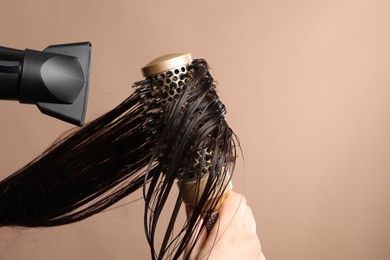 Photo of Hairdresser blow drying client's hair on light brown background, closeup. Space for text