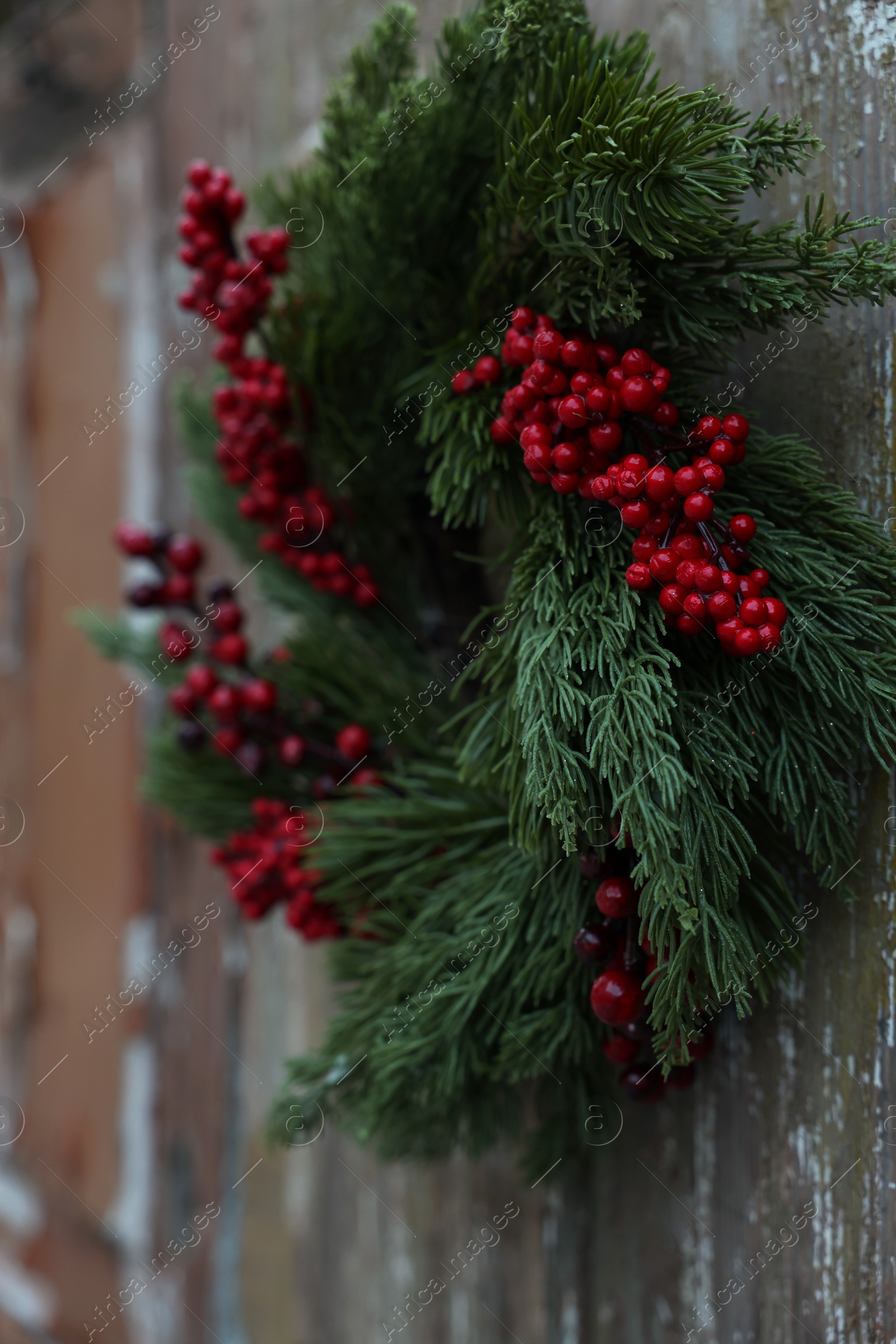 Photo of Beautiful Christmas wreath with red berries hanging on wooden wall, closeup