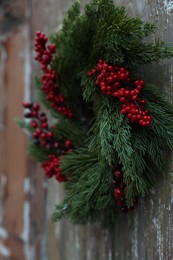 Photo of Beautiful Christmas wreath with red berries hanging on wooden wall, closeup