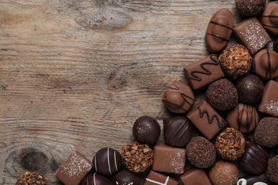 Different delicious chocolate candies on wooden table, flat lay. Space for text