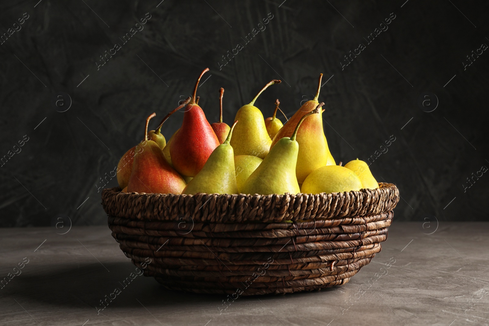 Photo of Wicker bowl with ripe pears on table against dark background