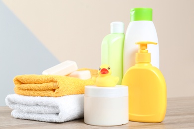 Baby cosmetic products, toy and towels on table against color background