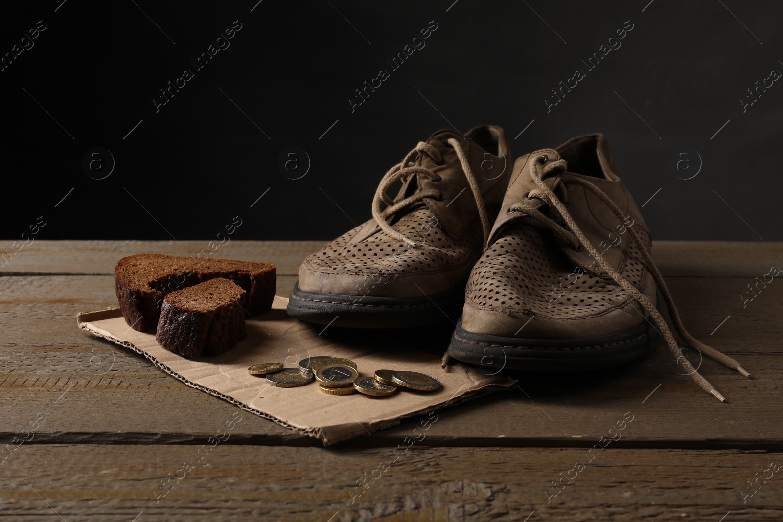 Photo of Poverty. Old shoes, coins, pieces of bread and cardboard sheet on wooden table