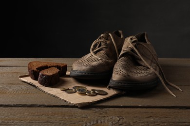 Poverty. Old shoes, coins, pieces of bread and cardboard sheet on wooden table