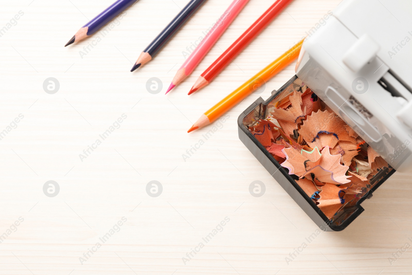 Photo of Mechanical sharpener with shavings near colorful pencils on white wooden table, flat lay. Space for text