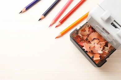 Photo of Mechanical sharpener with shavings near colorful pencils on white wooden table, flat lay. Space for text
