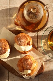 Photo of Delicious profiteroles filled with cream and tea on white tiled table, flat lay
