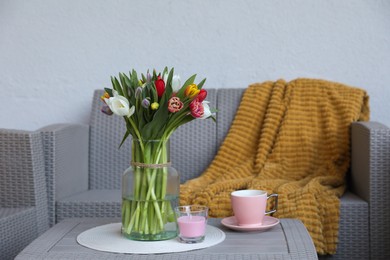 Photo of Beautiful bouquet of colorful tulips, cup with drink and candle on rattan garden table