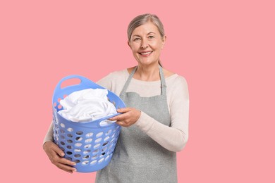 Happy housewife with basket full of laundry on pink background