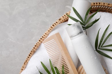 Dry shampoo sprays, towel and wooden comb with green leaves in wicker basket on light grey table, top view. Space for text