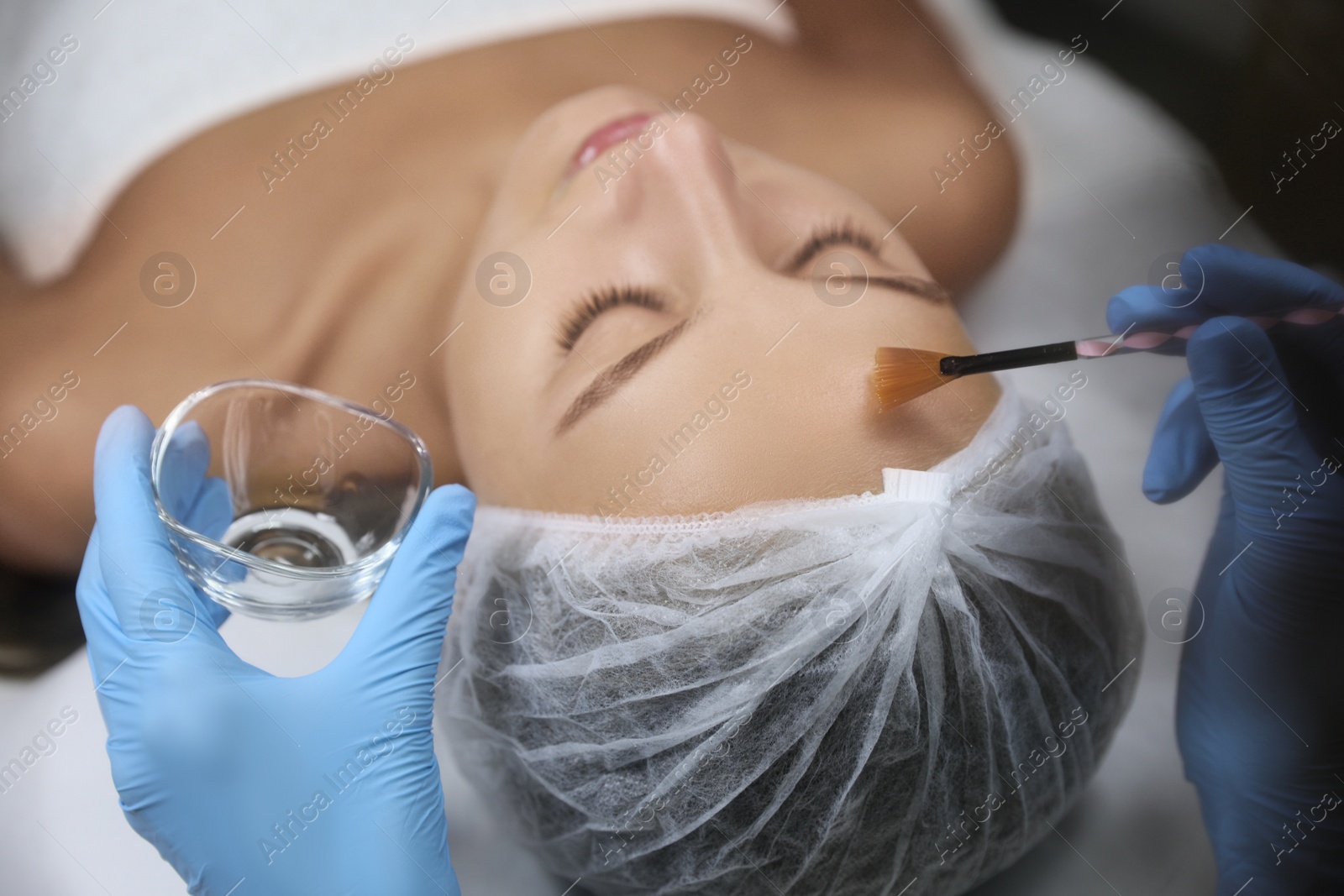 Photo of Cosmetologist applying chemical peel product on client's face in salon